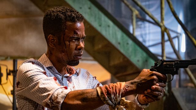 Chris Rock, crudely bandaged and spattered with blood, points a gun offscreen in Spiral: From the Book of Saw