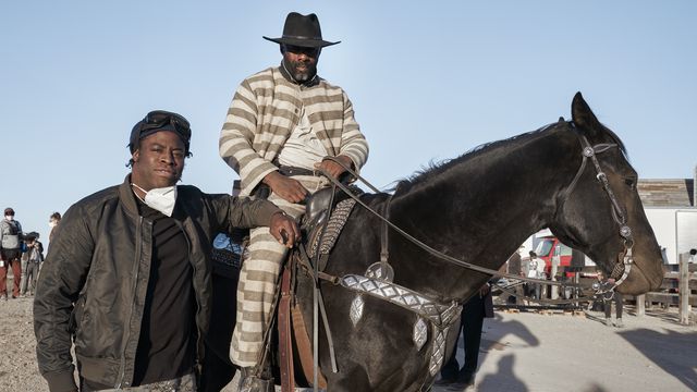 Director Jeymes Samuel and Idris Elba (in an Old West prisoner’s uniform, on a horse) on the set of The Harder They Fall
